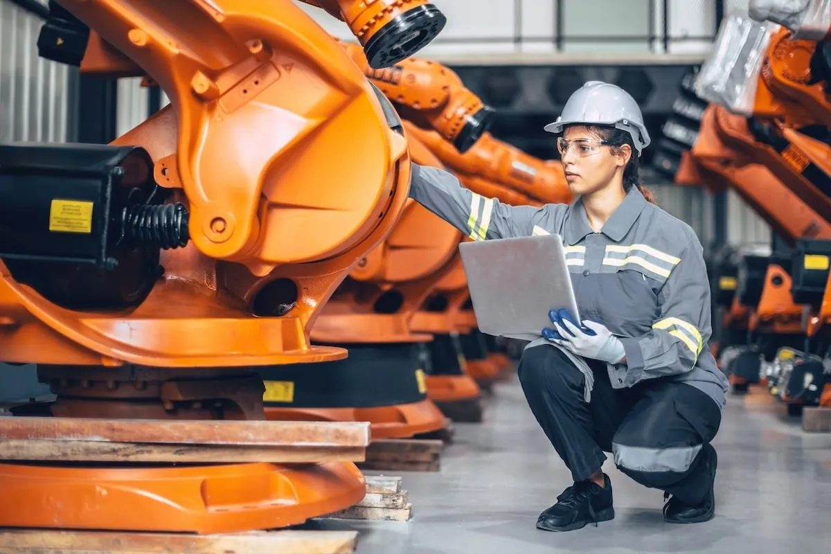 A female engineer in a hard hat inspecting robotics on a factory floor