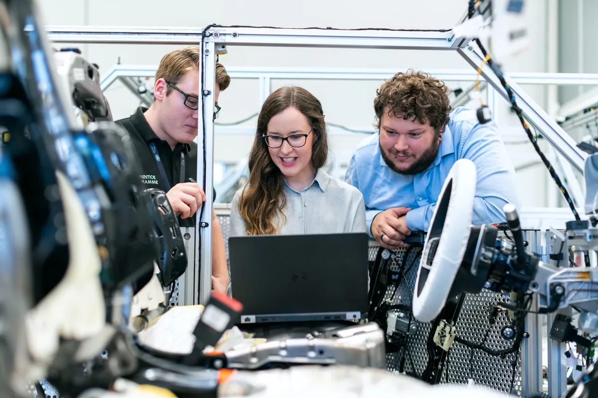 Colleagues gathered around a laptop working through a technical problem together